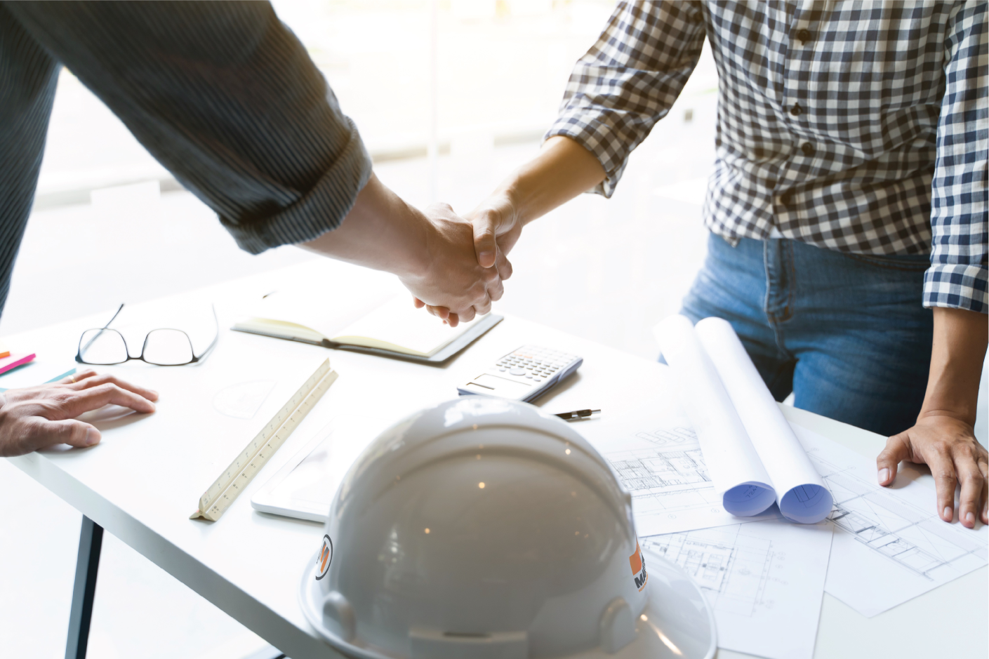 Poignée de main au-dessus de plans de projet et d'un casque de sécurité